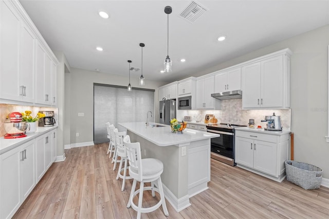 kitchen featuring white cabinets, decorative light fixtures, stainless steel appliances, and an island with sink