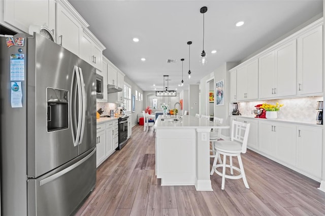 kitchen featuring a center island with sink, hanging light fixtures, tasteful backsplash, white cabinetry, and stainless steel appliances