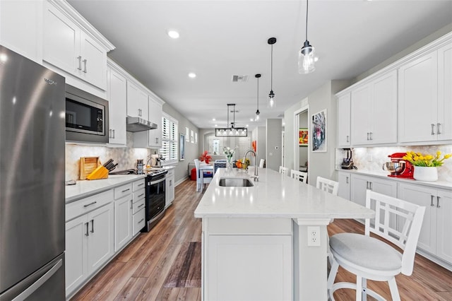 kitchen featuring decorative backsplash, stainless steel appliances, sink, decorative light fixtures, and a center island with sink