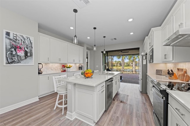 kitchen featuring stainless steel appliances, white cabinets, light hardwood / wood-style floors, hanging light fixtures, and an island with sink