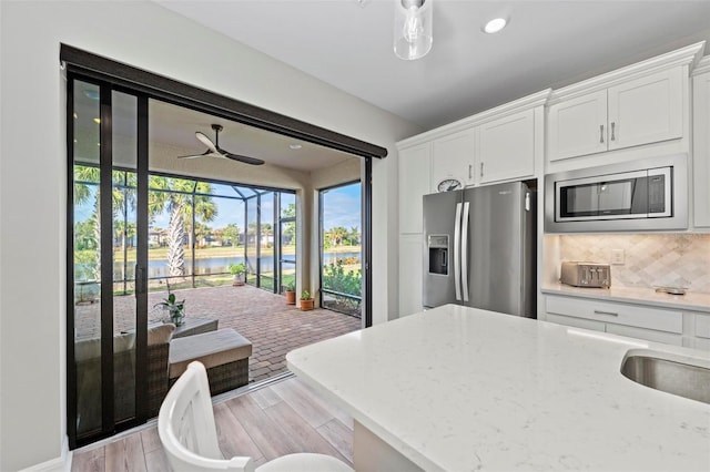 kitchen with a water view, appliances with stainless steel finishes, tasteful backsplash, light stone counters, and white cabinetry