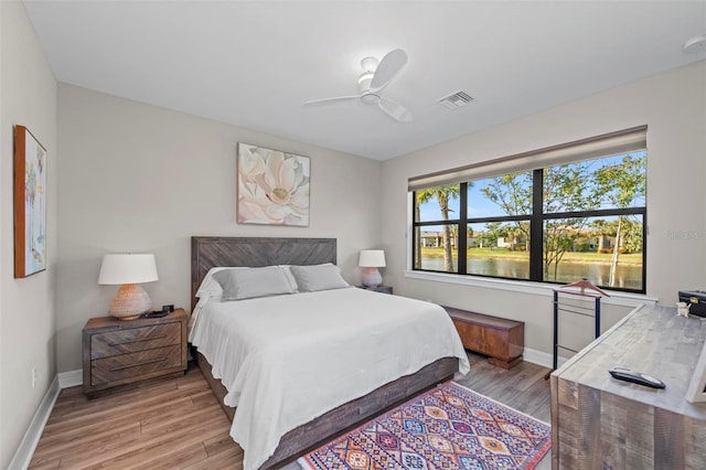 bedroom featuring a water view, light hardwood / wood-style flooring, and ceiling fan