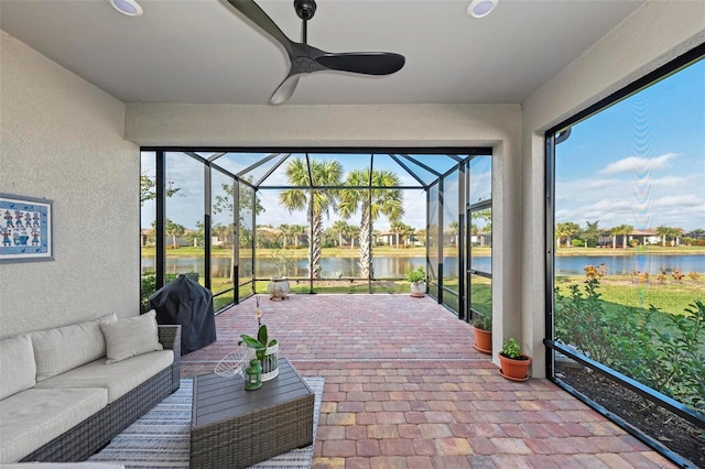 sunroom with ceiling fan and a water view