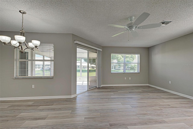 empty room with ceiling fan with notable chandelier, a textured ceiling, and light wood-type flooring