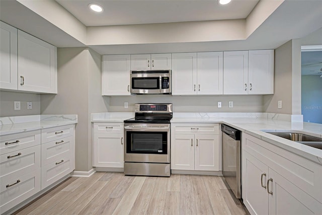 kitchen with white cabinetry, appliances with stainless steel finishes, light stone countertops, and light wood-type flooring