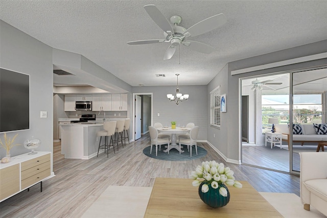 dining space featuring ceiling fan with notable chandelier, a textured ceiling, and light hardwood / wood-style flooring