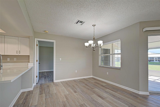 unfurnished dining area featuring a chandelier, a textured ceiling, and light wood-type flooring