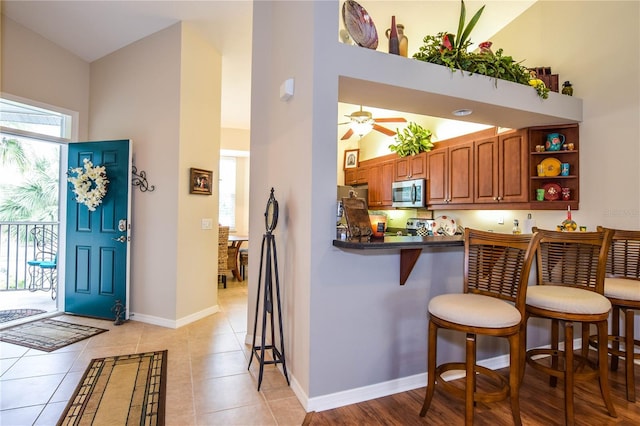 kitchen featuring kitchen peninsula, a towering ceiling, a breakfast bar, ceiling fan, and light tile patterned floors