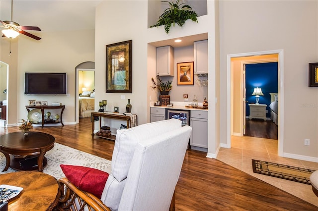 tiled living room with bar, ceiling fan, and a high ceiling