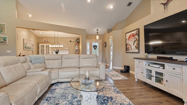 living room with a notable chandelier, dark hardwood / wood-style flooring, and vaulted ceiling