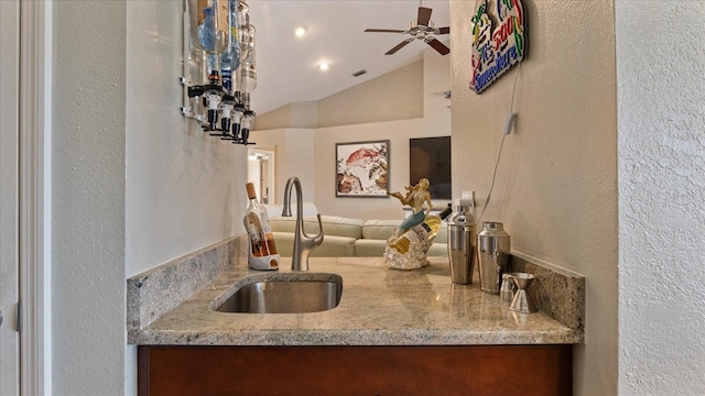 kitchen featuring light stone counters, ceiling fan, vaulted ceiling, and sink