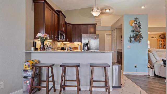 kitchen featuring stainless steel appliances, kitchen peninsula, light tile patterned floors, light stone counters, and tasteful backsplash