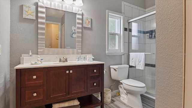 bathroom with toilet, a shower with door, and vanity