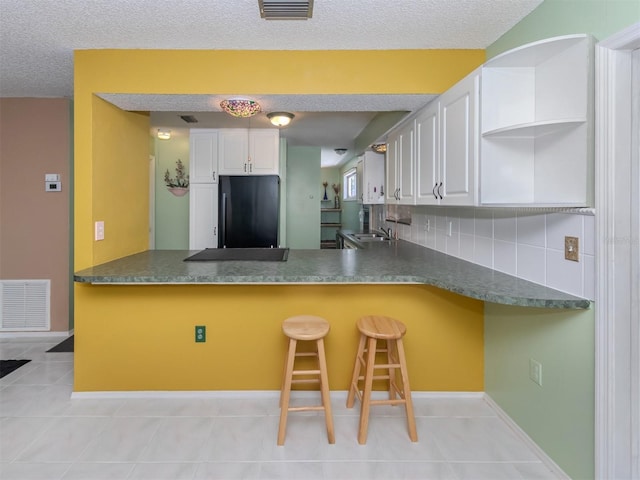 kitchen with white cabinets, black fridge, kitchen peninsula, decorative backsplash, and a breakfast bar