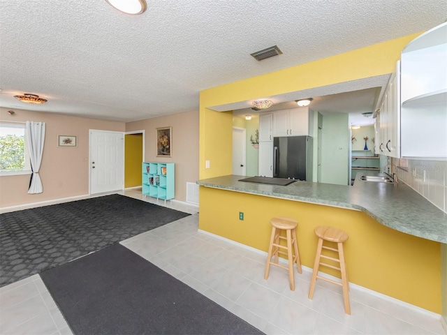 kitchen featuring white cabinets, light tile patterned floors, kitchen peninsula, stainless steel fridge, and a breakfast bar