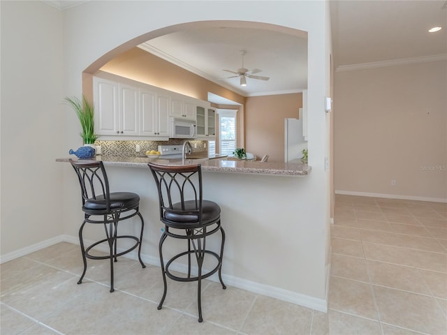 kitchen with light tile patterned floors, a breakfast bar area, fridge, white cabinets, and decorative backsplash