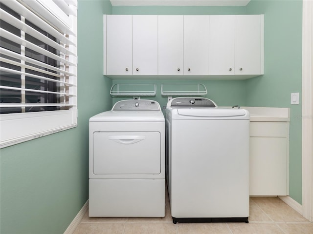 clothes washing area with light tile patterned floors, washing machine and dryer, and cabinets