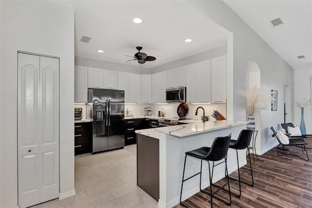 kitchen featuring kitchen peninsula, stainless steel appliances, white cabinets, ceiling fan, and a kitchen breakfast bar