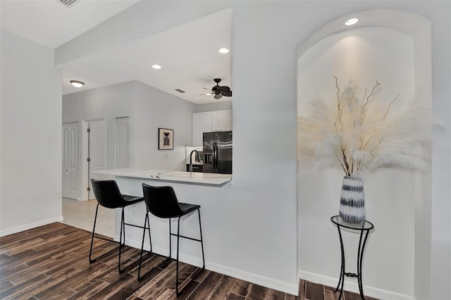 kitchen featuring kitchen peninsula, stainless steel fridge with ice dispenser, a kitchen bar, white cabinets, and ceiling fan