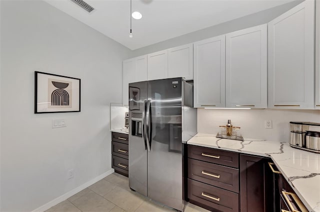 kitchen featuring light tile patterned floors, light stone counters, stainless steel refrigerator with ice dispenser, white cabinets, and dark brown cabinets