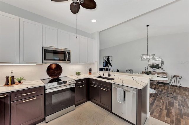 kitchen with vaulted ceiling, appliances with stainless steel finishes, kitchen peninsula, sink, and white cabinetry