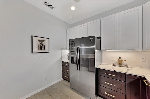 kitchen with light stone countertops, light tile patterned floors, stainless steel refrigerator with ice dispenser, white cabinetry, and tasteful backsplash