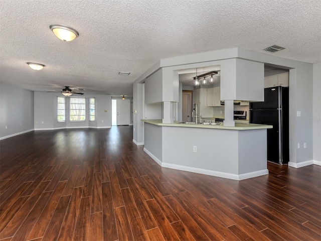 kitchen with ceiling fan, dark hardwood / wood-style floors, black fridge, kitchen peninsula, and white cabinets