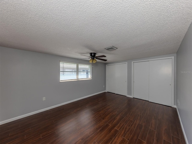 unfurnished bedroom featuring ceiling fan, dark hardwood / wood-style flooring, a textured ceiling, and two closets