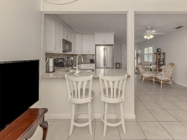 kitchen with appliances with stainless steel finishes, tasteful backsplash, light stone counters, ceiling fan, and white cabinets