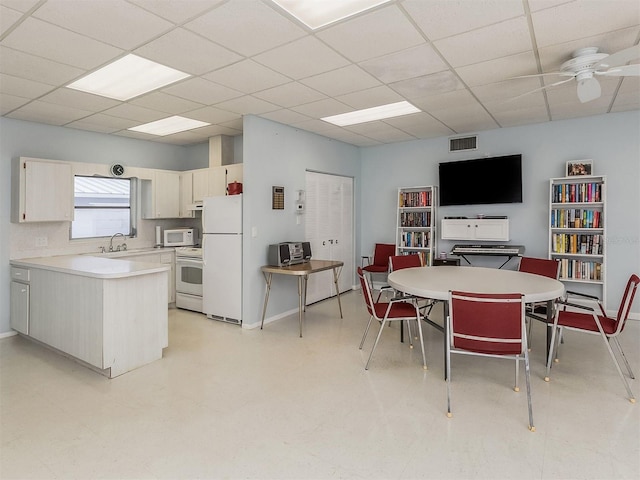 kitchen with a drop ceiling, a kitchen island, white appliances, and ceiling fan