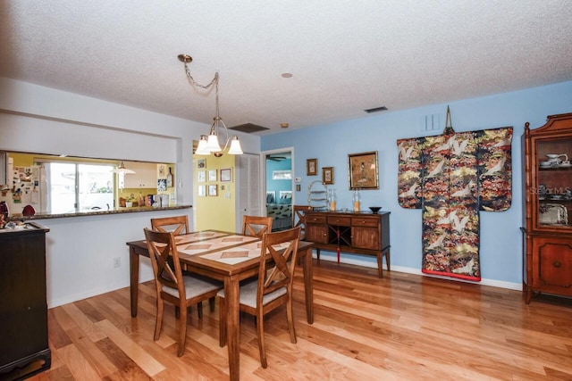 dining area featuring light hardwood / wood-style floors, a textured ceiling, and a chandelier