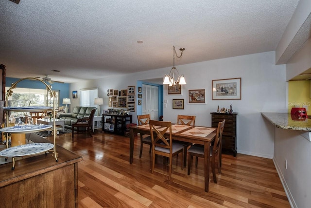 dining space with a textured ceiling, ceiling fan with notable chandelier, and hardwood / wood-style flooring