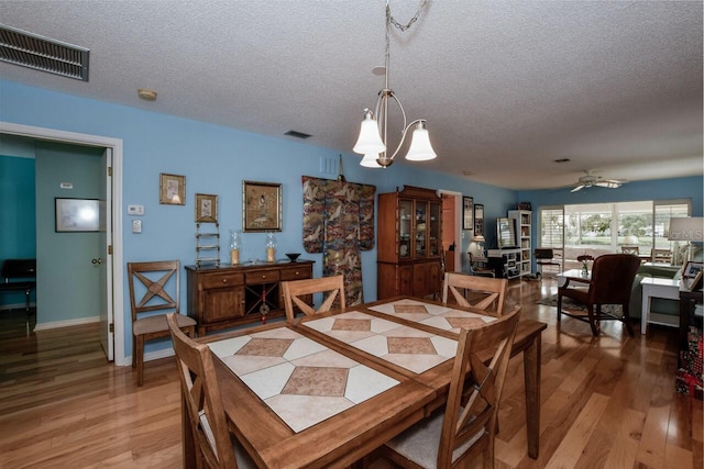 dining room with hardwood / wood-style floors, ceiling fan with notable chandelier, and a textured ceiling