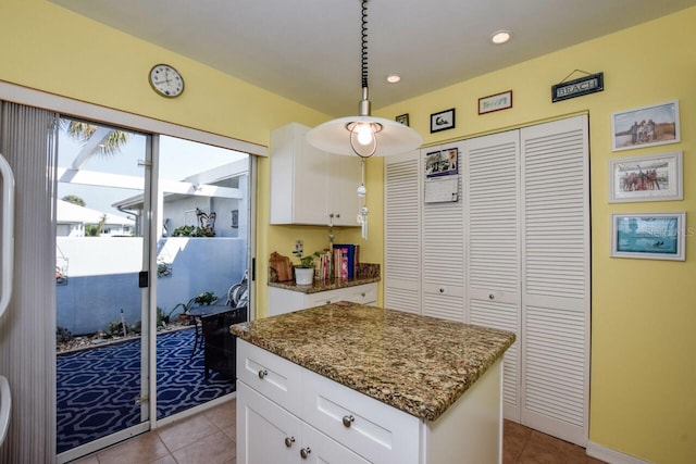 kitchen featuring pendant lighting, a center island, light tile patterned floors, light stone counters, and white cabinetry