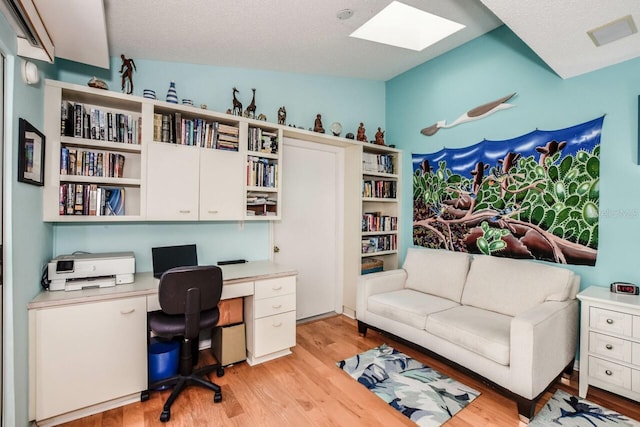 home office with a textured ceiling, light wood-type flooring, and built in desk