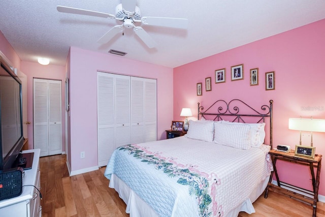 bedroom with two closets, light hardwood / wood-style flooring, and ceiling fan