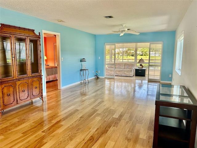 interior space featuring a textured ceiling, ceiling fan, light wood-style flooring, baseboards, and visible vents