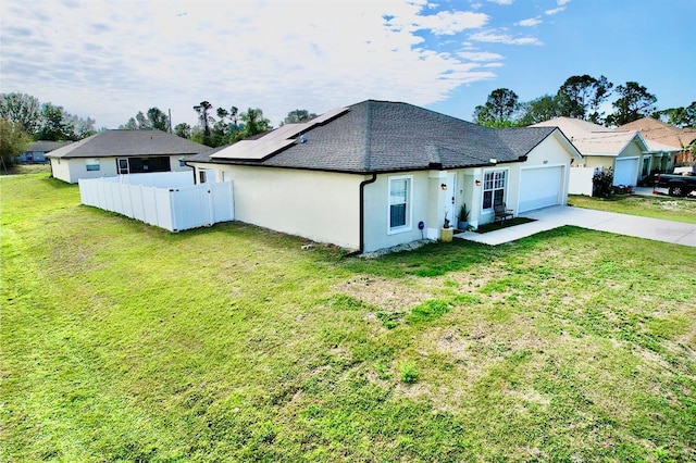 rear view of property featuring a garage, a lawn, and solar panels