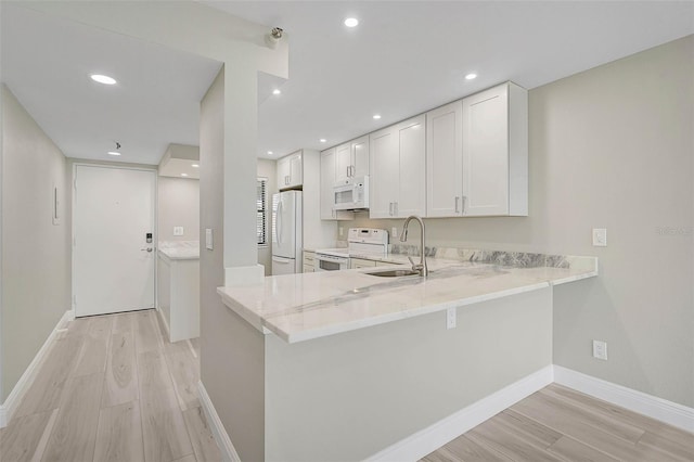 kitchen with white appliances, white cabinets, sink, kitchen peninsula, and light hardwood / wood-style flooring