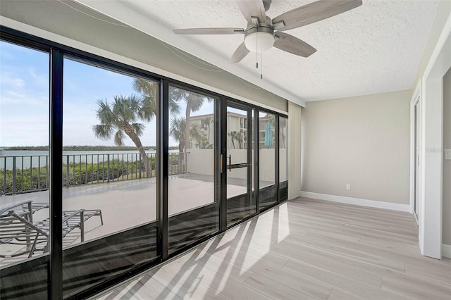 doorway featuring a water view, ceiling fan, light wood-type flooring, and a textured ceiling