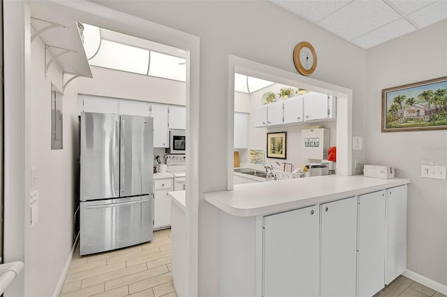 kitchen with white cabinetry, stainless steel fridge, kitchen peninsula, and a drop ceiling