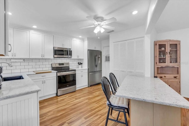 kitchen featuring light stone counters, stainless steel appliances, backsplash, white cabinets, and sink