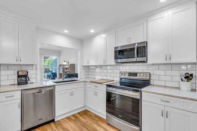 kitchen with stainless steel appliances, white cabinets, backsplash, and light hardwood / wood-style flooring