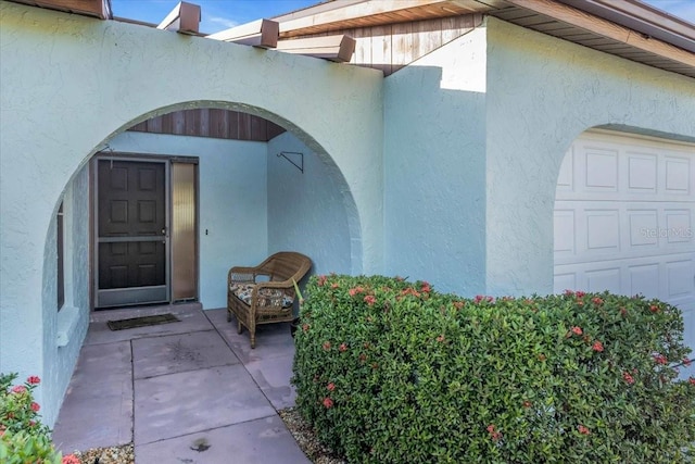 view of exterior entry with an attached garage and stucco siding