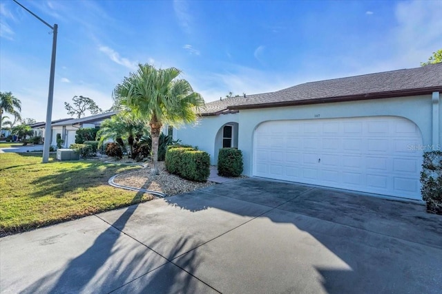 view of front of property featuring stucco siding, a front lawn, a garage, and driveway