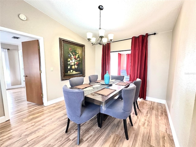 dining area with light hardwood / wood-style floors, a textured ceiling, lofted ceiling, and a chandelier