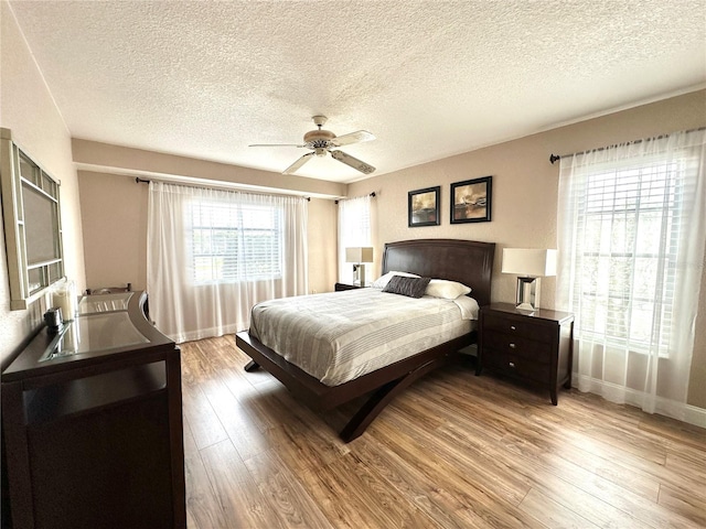 bedroom with light wood-type flooring, ceiling fan, and a textured ceiling