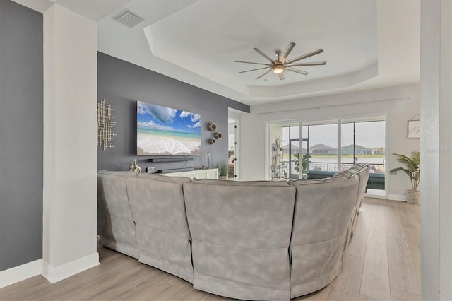 living room featuring light hardwood / wood-style flooring, a raised ceiling, and ceiling fan