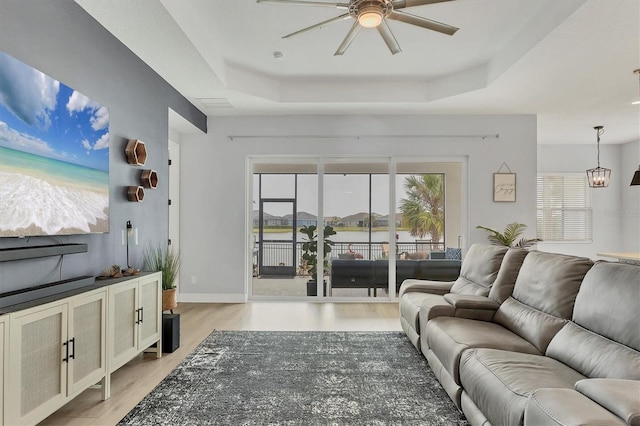 living room with a tray ceiling, light hardwood / wood-style flooring, and plenty of natural light