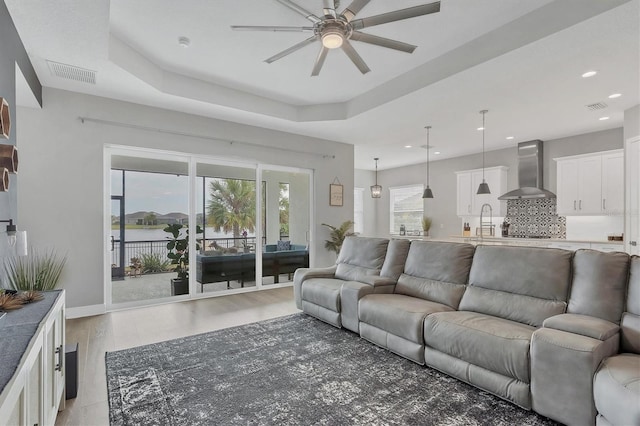 living room with a raised ceiling, ceiling fan, light hardwood / wood-style flooring, and sink